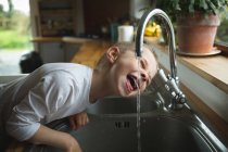 Junge trinkt zu Hause Wasser aus Wasserhahn in Küche — Stockfoto