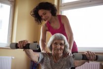 Женщина-терапевт помогает пожилой женщине с гантелями в доме престарелых — стоковое фото