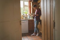 Человек с помощью мобильного телефона и держа чашку кофе на кухне дома . — стоковое фото