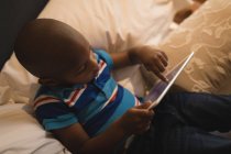 Hochwinkelaufnahme eines Jungen, der im Schlafzimmer mit einem digitalen Tablet spielt. — Stockfoto
