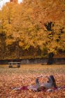 Femme couchée dans le parc et lisant un roman à l'automne — Photo de stock