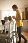 Мати дивиться, як діти використовують ноутбук на кухні вдома — стокове фото