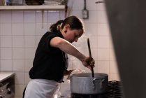 Шеф-кухар перемішуючи під час приготування їжі на комерційній кухні — стокове фото