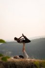 Pareja deportiva practicando acro yoga en un exuberante terreno verde en el momento de dwan - foto de stock