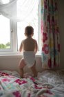 Visão traseira da menina de pé perto da janela em casa — Fotografia de Stock
