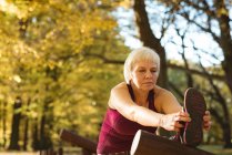 Senior woman performing stretching exercise in the park on a sunny day — Stock Photo