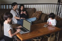 Boy using laptop while mother and daughter sitting in background at home — Stock Photo