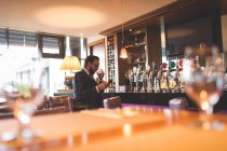 Geschäftsmann benutzt Handy, während er Whiskey in Bar trinkt — Stockfoto