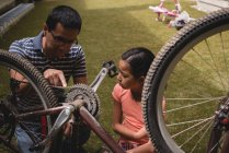 Father and daughter interacting with each other while repairing cycle in the garden — Stock Photo