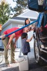 Pai e crianças se divertindo ao lavar o carro fora da garagem — Fotografia de Stock