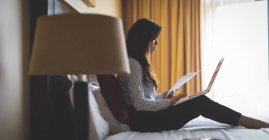 Бизнесмен читает документы во время работы на ноутбуке в гостиничном номере — стоковое фото