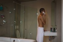 Jovem aplicando creme de barbear em seu rosto no banheiro — Fotografia de Stock