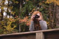 Рыжая женщина фотографирует в осеннем лесу — стоковое фото