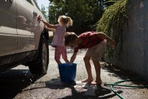 Hermanos lavando un coche en el garaje exterior en un día soleado - foto de stock