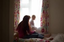 Mutter mit ihrem kleinen Mädchen, das zu Hause durch das Fenster schaut — Stockfoto
