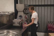 Женщина-работница наливает джин в бутылку с машины на заводе — стоковое фото