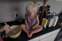 Menina da criança assistindo como irmão preparando comida na cozinha em casa . — Fotografia de Stock