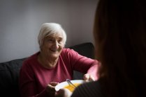 Nonna sorridente che riceve il piatto di minestra da nipote in soggiorno — Foto stock
