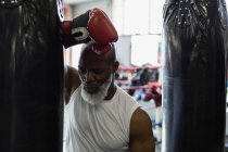 Close-up of tired senior boxer leaning against punching bag. — Stock Photo