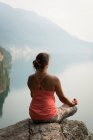 Fit woman sitting in meditating posture on the edge of a rock at the time of dawn — Stock Photo