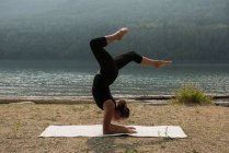 Donna in forma facendo yoga acrobatico vicino alla costa del mare in una giornata di sole — Foto stock