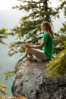 Fit man sitting in meditating posture on the edge of a rock at the time of dawn — Stock Photo