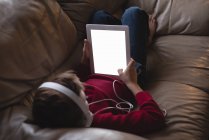 Niño usando tableta digital con auriculares en la sala de estar en casa - foto de stock