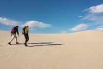Пара с рюкзаком, идущим по песку в солнечный день — стоковое фото