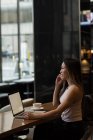 Empresária falando ao telefone enquanto trabalhava em laptop na cafeteria — Fotografia de Stock