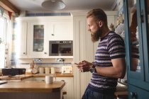 Man lining on shelf while using mobile phone in kitchen — Stock Photo