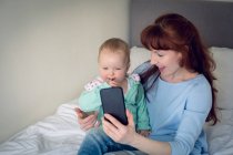 Мати і дитина дівчинка бере селфі з мобільним телефоном в спальні вдома — стокове фото