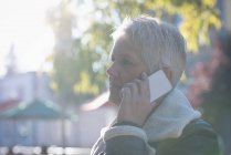 Вид збоку на старшу жінку, що розмовляє по мобільному телефону в сонячний день — стокове фото
