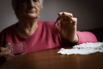 Partie médiane de la femme âgée regardant la médecine dans le salon à la maison — Photo de stock