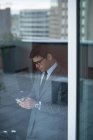 Бізнесмен використовує мобільний телефон біля скляного вікна — стокове фото
