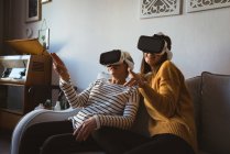 Seniorin und Tochter tragen ein Virtual-Reality-Headset, während sie sich auf einem Sofa entspannen — Stockfoto