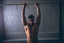 Muscular man exercising on pull-up bar in the fitness studio — Stock Photo