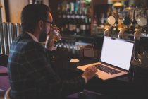 Бизнесмен использует ноутбук, когда пьет виски в баре — стоковое фото