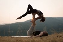 Sporty couple practicing acro yoga in a lush green ground at the time of dwan — Stock Photo