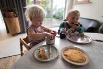 Crianças tendo panquecas como café da manhã na sala de estar em casa . — Fotografia de Stock
