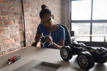 Girl repairing drone and electric model car in office. — Stock Photo