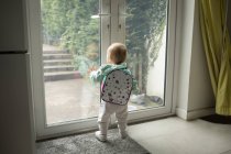 Vue arrière de bébé fille avec cartable regardant par la porte — Photo de stock