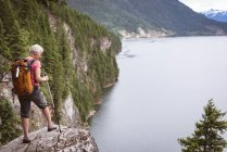 Mature woman with hiking poles standing on rock — Stock Photo