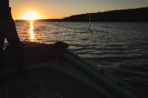 Abgeschnittene Ansicht eines Mannes beim Angeln, während er bei Sonnenuntergang auf einem Motorboot im Fluss steht. — Stockfoto
