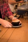 Sección media de barista hembra sirviendo café en el mostrador en la cafetería - foto de stock