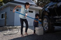 Siblings washing car together outside garage on a sunny day — Stock Photo