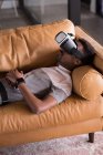 Young man experiencing VR headset while lying on sofa — Stock Photo