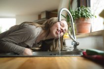 Jovem garota bebendo água da torneira na cozinha em casa — Fotografia de Stock