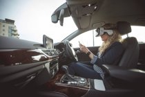 Side view of female executive using digital tablet and virtual reality headset in a car — Stock Photo