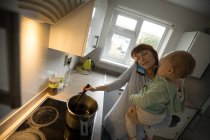 Mother talking on mobile phone while holding her baby girl in the kitchen at home — Stock Photo