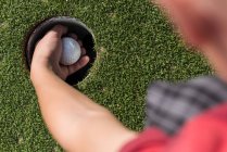 Vista de ángulo alto del niño quitando la pelota de golf del agujero en el campo - foto de stock